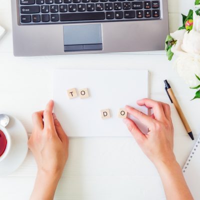 A person sitting in front of their laptop with a cup of coffee spelling out "To-Do" on white card